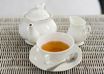 Cup of tea with little milk jar and teapot