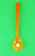Plastic spoons with color pills on green background