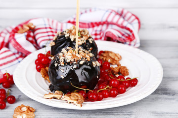 Sweet caramel apples on sticks with berries, on wooden table