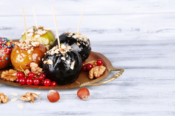 Sweet caramel apples on sticks with berries, on wooden table
