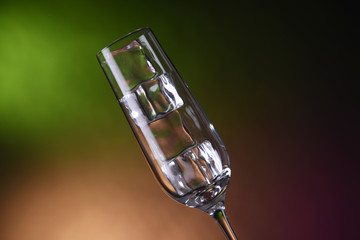 Glass with ice cubes on color background