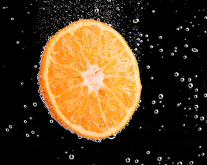 Fresh orange in water with bubbles on black background