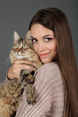 Beautiful young woman holding cat on gray background