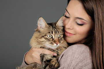 Beautiful young woman holding cat on gray background