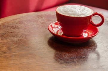 red coffee mug with frothed milk on an old wooden table