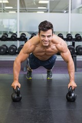 Fototapeta na wymiar Muscular man doing push ups with kettle bells in gym