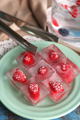 Obraz na płótnie Canvas Ice cubes with raspberry on plate, on color wooden background