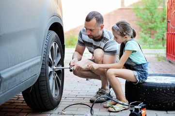 Cute  girl helps her father to change wheel  - obrazy, fototapety, plakaty