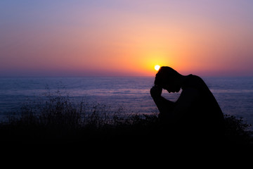 Man Praying by the Sea at Sunset - obrazy, fototapety, plakaty