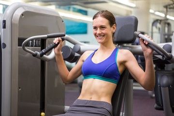 Fototapeta na wymiar Fit smiling brunette using weights machine for arms