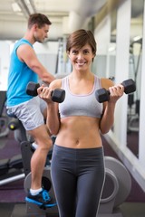 Fototapeta na wymiar Fit brunette lifting weights smiling at camera