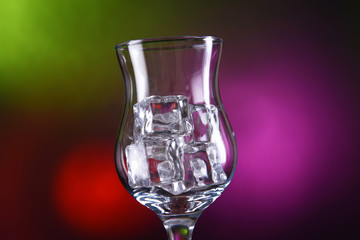 Glass with ice cubes on color background