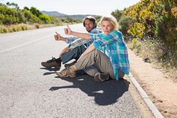 Obraz premium Attractive couple sitting on the road hitching a lift