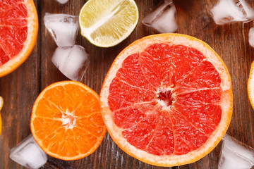 Different sliced juicy citrus fruits with ice on wooden table