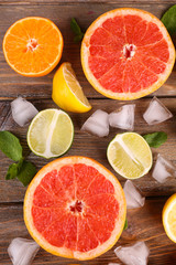 Different sliced juicy citrus fruits with ice on wooden table