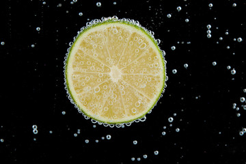 Fresh lime in water with bubbles on black background
