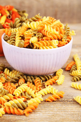 Assortment of colorful pasta in color bowls on wooden