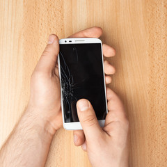 Hands holding a phone with a broken screen