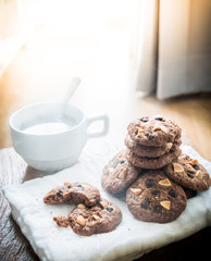 Chocolate chip cookies on napkin and hot tea on wooden table.