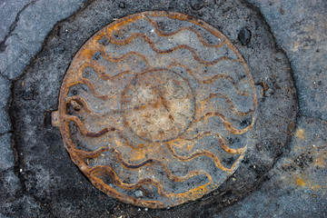 Manhole with rusty metal cover in cracked asphalt surface