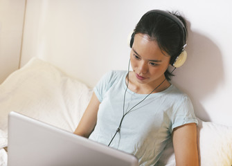 Casual young woman sitting on bed and using laptop at home.