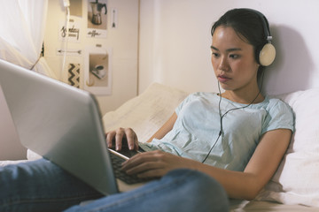 Casual young woman lying on bed and using laptop at home.