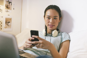 Casual young woman sitting on bed and using smart phone at home.