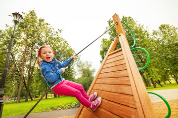 Funny girl climbs by rope on wooden construction