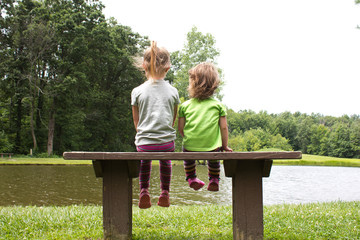 Sisters sitting on a bench at a pond