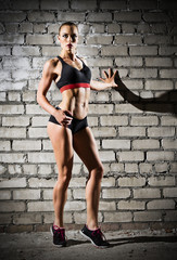 Muscular woman on brick wall (dark version)