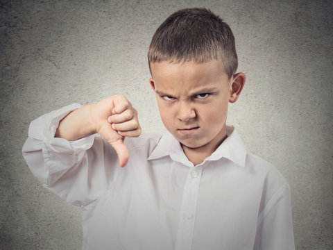 Angry boy giving thumbs down hand gesture, grey background 