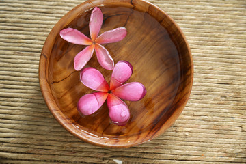 Obraz na płótnie Canvas frangipani in water wooden bowl on Brown straw mat