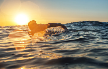 Fototapeta premium Młodego człowieka dopłynięcie w morzu nad żółtym wschodem słońca