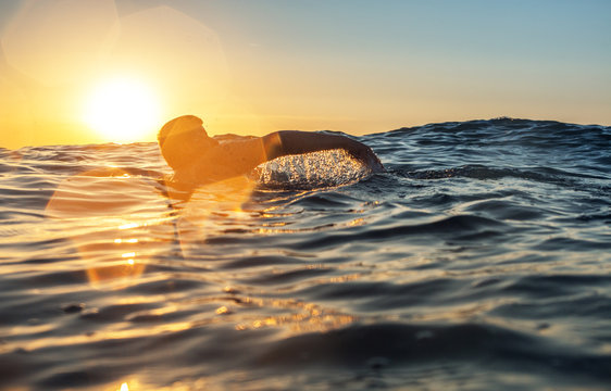 Fototapeta Young man swiming in the sea over yellow sunrise