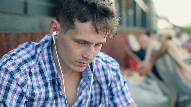 Young trendy man listen to music on smartphone in outdoor bar
