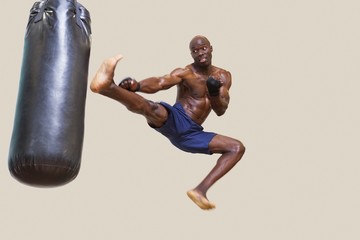Shirtless muscular boxer kicking punching bag