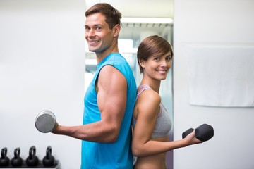 Obraz premium Fit couple lifting dumbbells together smiling at camera