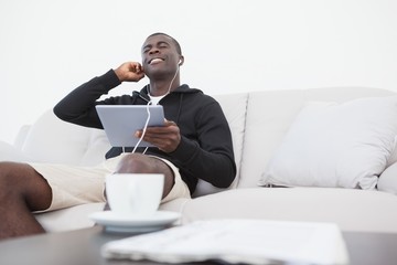 Casual man sitting on sofa enjoying music on his tablet pc