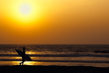 Naklejka na ściany i meble man walking along the coast with surfboard at the sunset