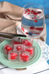 Ice cubes with raspberry on plate, on color wooden background
