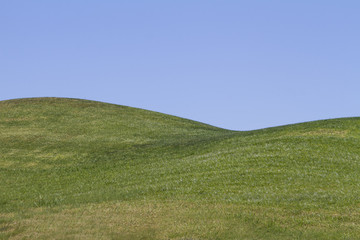 Uitzicht op kale groene heuvels met een blauwe lucht.