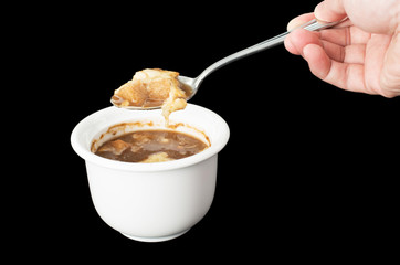 Hand holding spoon with cheese on onion soup isolated on black b