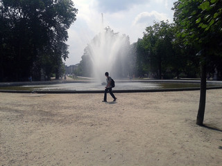 Jeune homme marchant dans le parc devant le jet d'eau