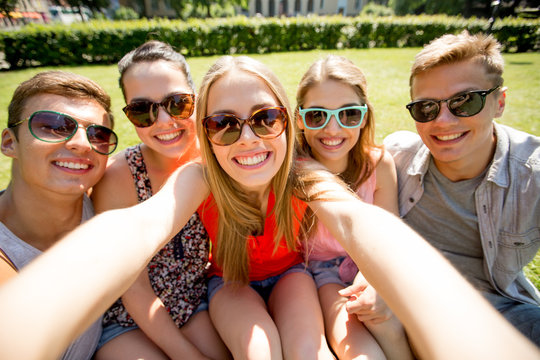 group of smiling friends making selfie in park