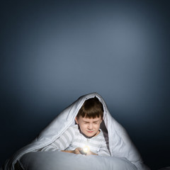 boy under the covers with a flashlight