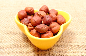 Fototapeta premium Heap of hazelnut in yellow cup on jute canvas