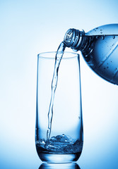 Pouring water into glass  from bottle on blue background