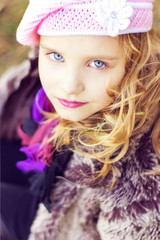 little girl with blue eyes in the pink hat sitting in the forest