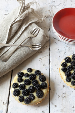 two blackberries tart with pastry cream on wooden table