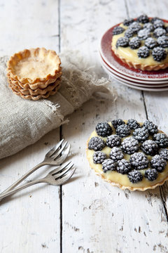 two homemade blackberries tart with pastry cream on wooden table